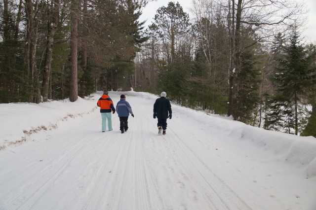 Three women in winter gear at an RVAA retreat walking down a snowy trail
